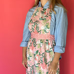 Person wearing Madcap Cottage Floral   apron over a blue shirt against a red background