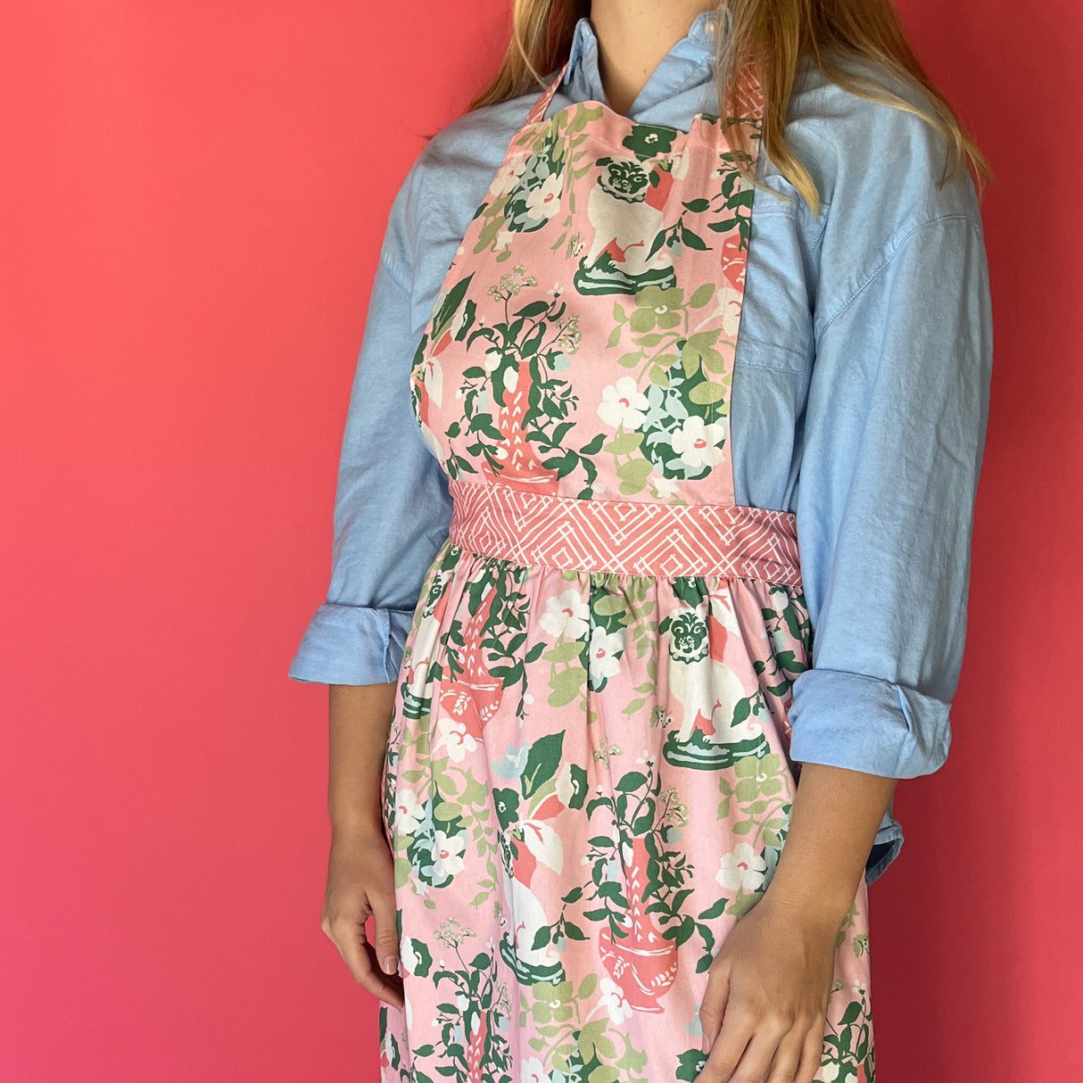 Person wearing Madcap Cottage Floral   apron over a blue shirt against a red background