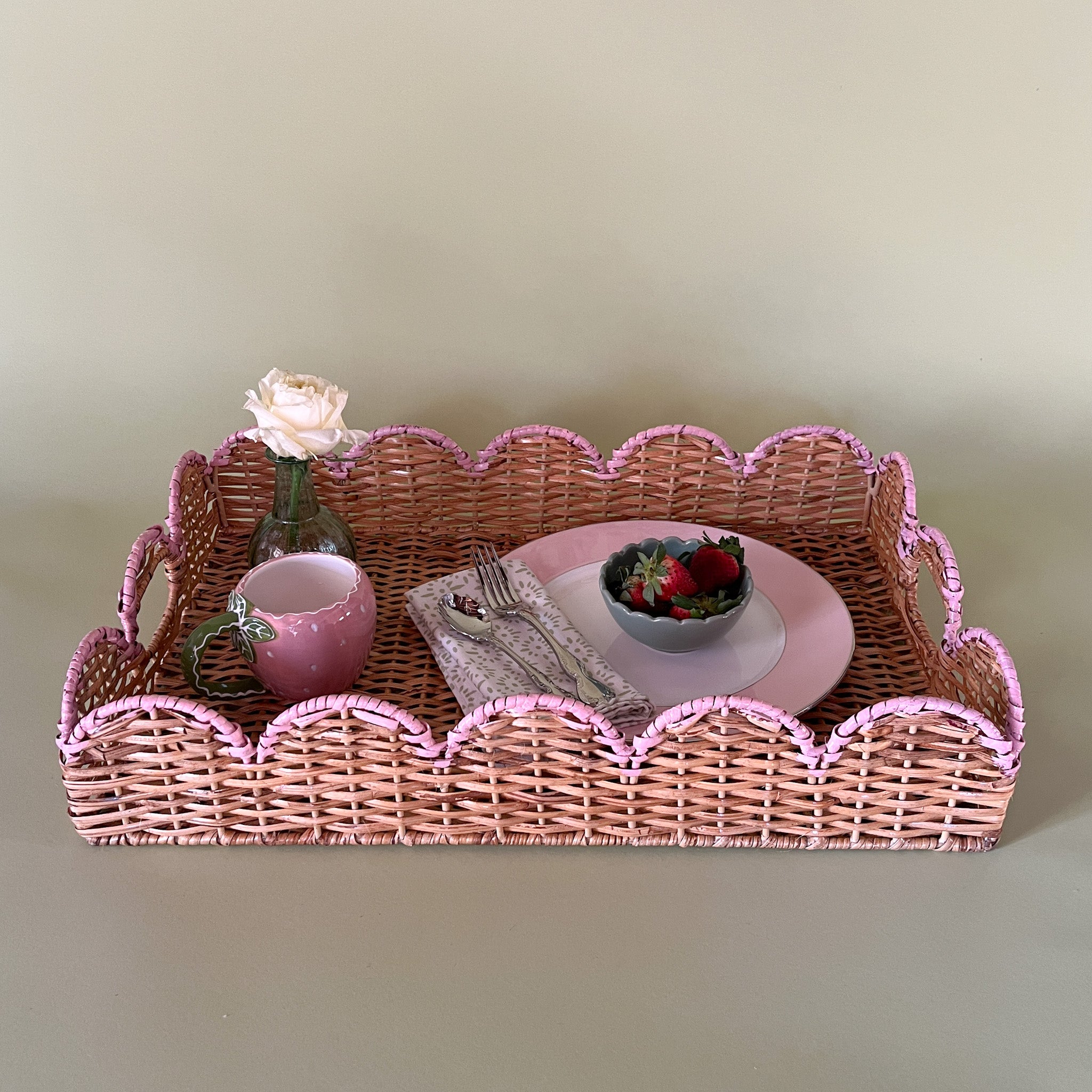 syled rattan tray with a pink scalloped edge holding a plate, mug, bud vase