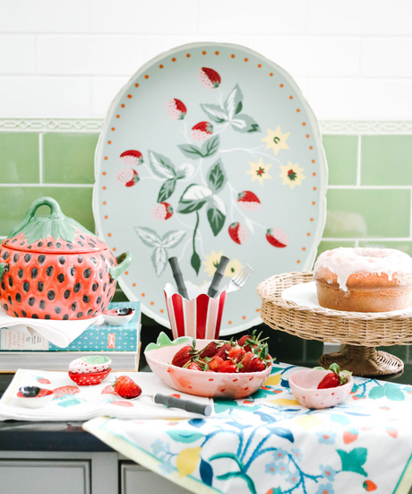 A kitchen scene featuring strawberry decor products such as a strawberry tray strawberry bowls, small strawberry dishes and strawberries and cake.