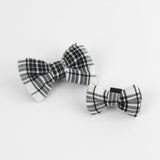2 MacLoecke Black/White Plaid Dog/Cat Bowties in Medium and Large placed on a white surface