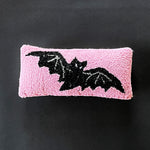 A pink wool lumbar accent pillow with a hooked design featuring a black bat silhouette.