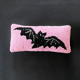 A pink wool lumbar accent pillow with a hooked design featuring a black bat silhouette.