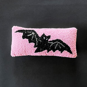 A pink wool lumbar accent pillow with a hooked design featuring a black bat silhouette.