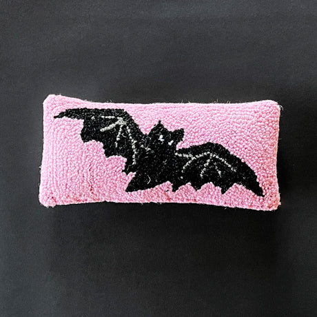 A pink wool lumbar accent pillow with a hooked design featuring a black bat silhouette.