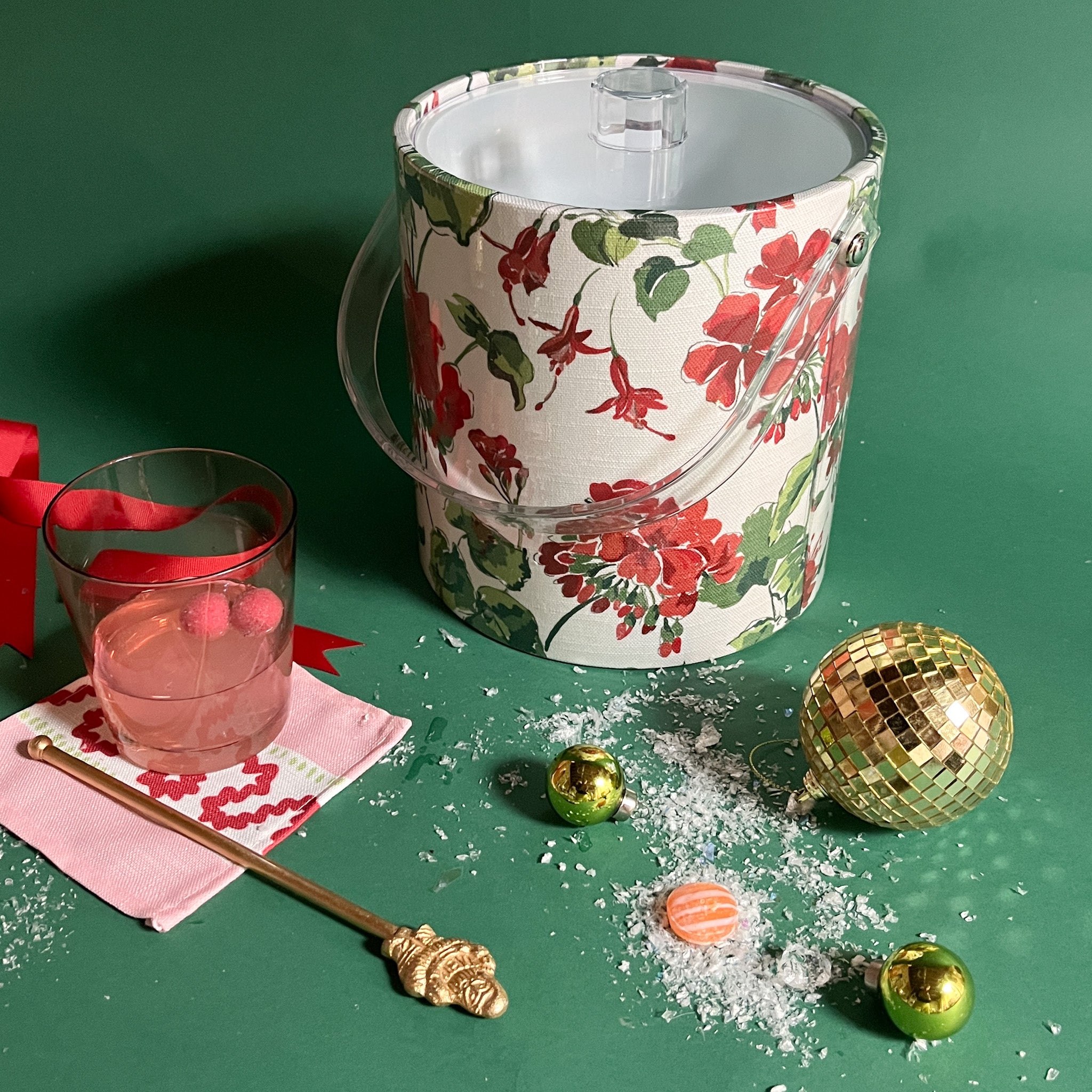 Cottage Grove Geranium is an acrylic ice bucket covered in red geranium fabric and surrounded by a cocktail and festive decorations.