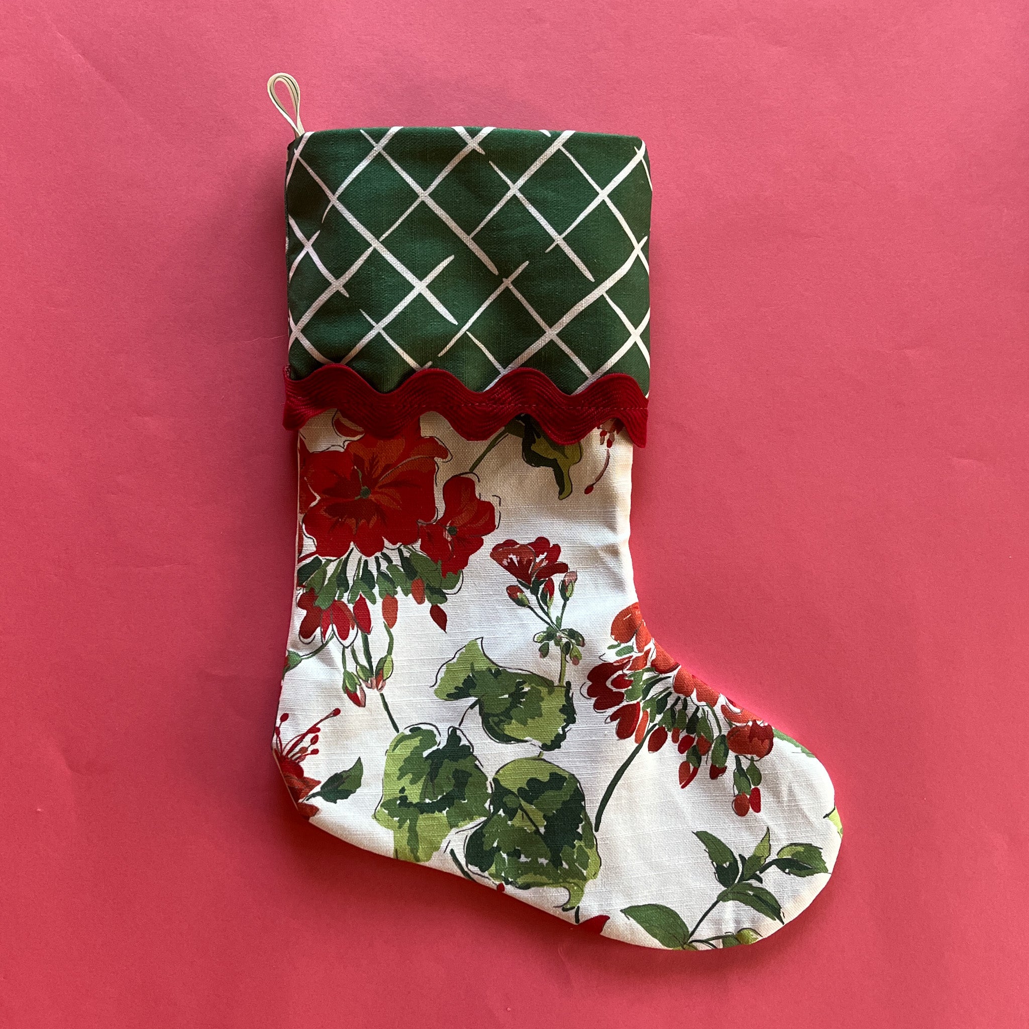 A Green, white and red Christmas stocking in a geranium print with a green geometric folded top