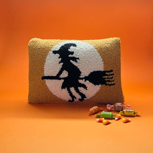 Madcap Cottage black witch riding a broomstick orange Halloween throw pillow on an orange background with candy cane in foreground.
