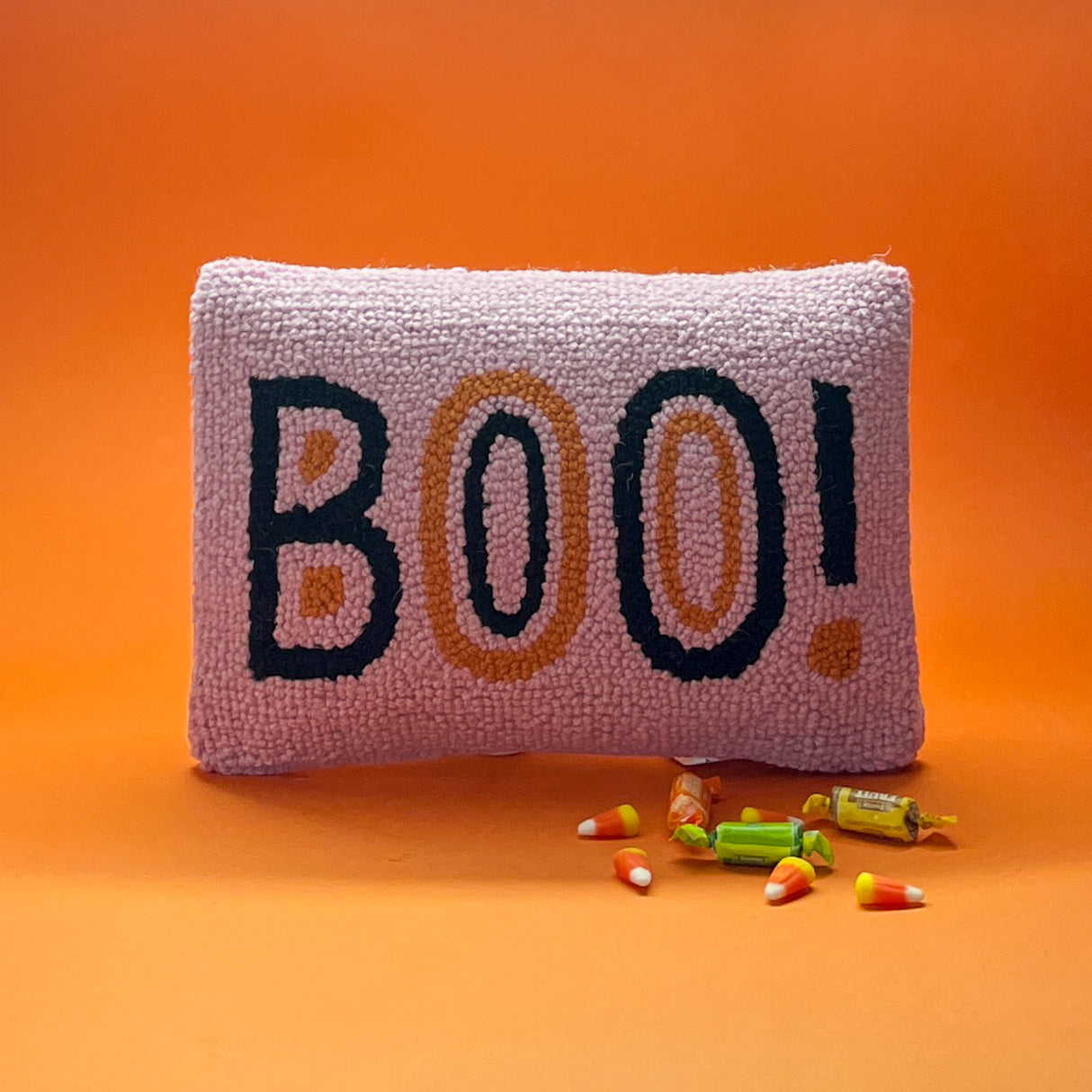 Madcap Cottage Pink halloween throw pillow with black and orange text that says Boo on an orange background with halloween candy in foreground.