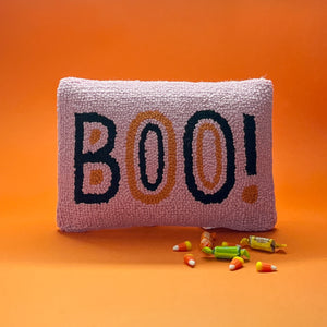 Madcap Cottage Pink halloween throw pillow with black and orange text that says Boo on an orange background with halloween candy in foreground.