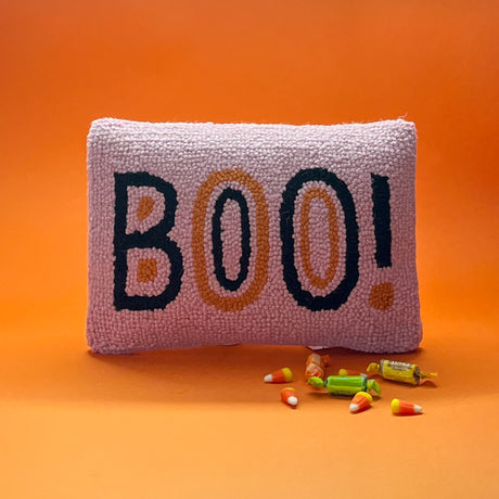 Madcap Cottage Pink halloween throw pillow with black and orange text that says Boo on an orange background with halloween candy in foreground.