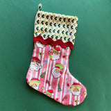 A pink christmas stocking made from pink santa motif fabric and a green patterned top with red ric rac trim