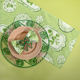 Green Society Hill Vintage Plates cloth table runner with matching napkin in a rattan napkin ring resting on a pink plate and green rattan placemat.