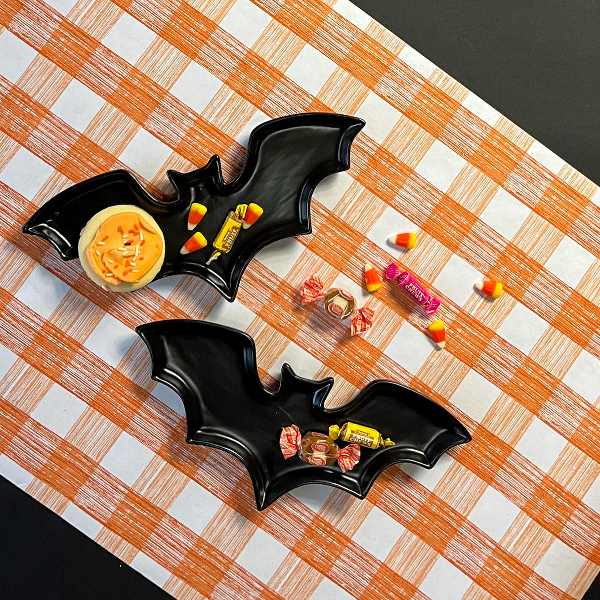 Madcap cottage black bat shaped halloween plates resting on orange gingham paper table runner