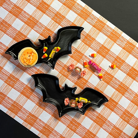 Madcap cottage black bat shaped halloween plates resting on orange gingham paper table runner