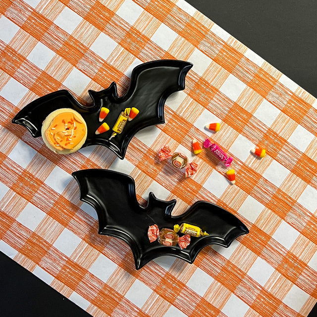 Madcap cottage black bat shaped halloween plates resting on orange gingham paper table runner