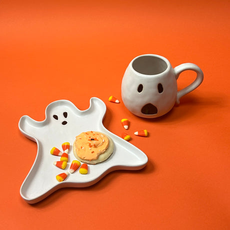 One ceramic mug with a white ghost design, one with a handle, with white plate on the side