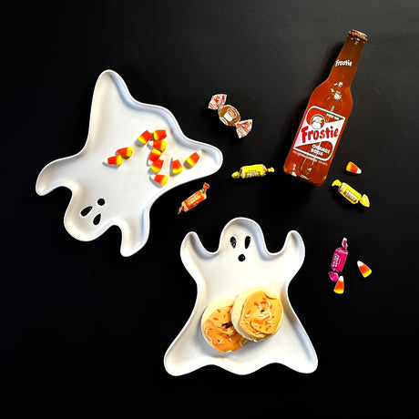 Two Madcap cottage ghost shaped ceramic halloween plates on a black background with halloween cookies and candies.