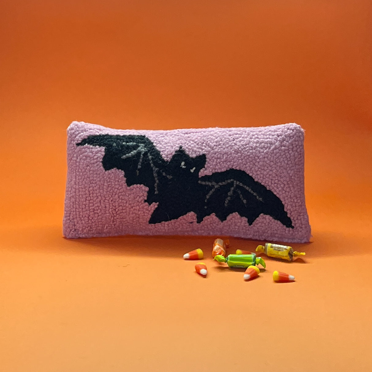 A pink wool halloween accent pillow with black bat design