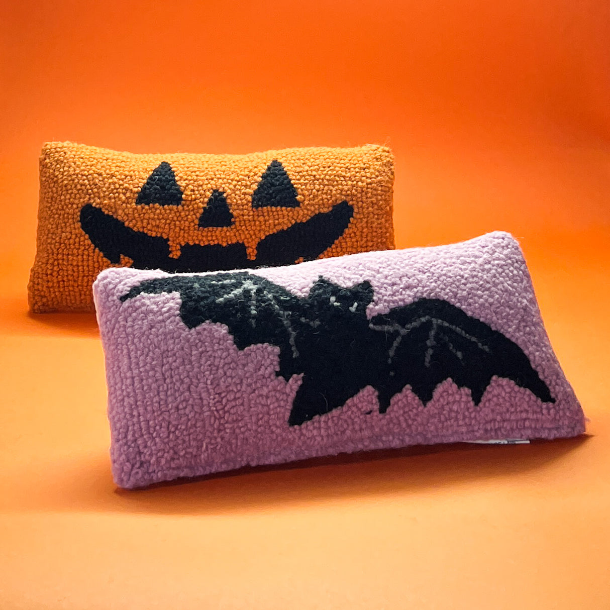 A pink wool lumbar halloween accent pillow with black bat design. another pillow with jack o lantern design