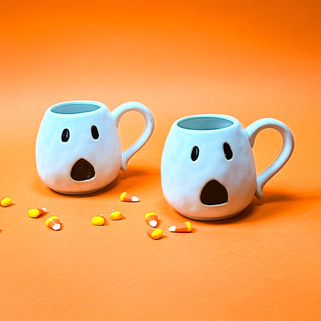 Two ceramic mugs with a white ghost design, one with a handle.