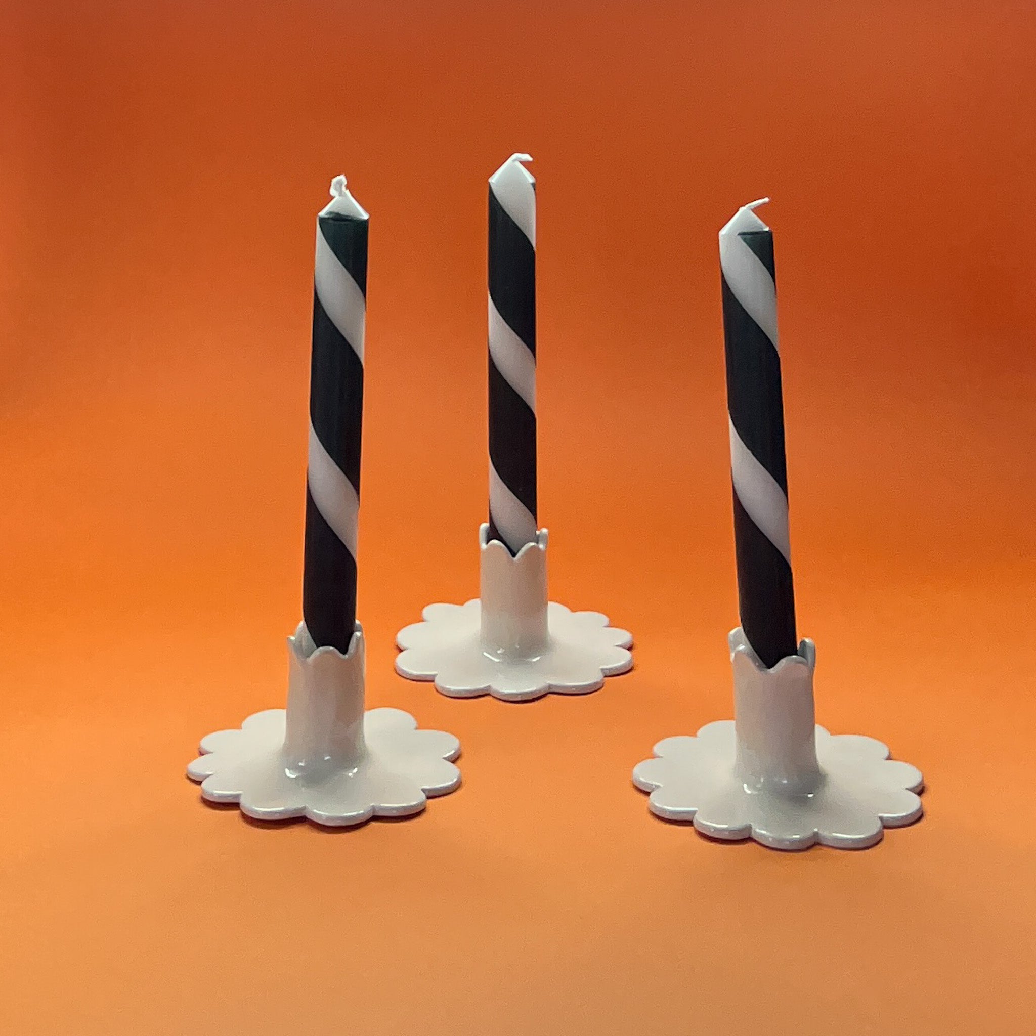 Madcap cottage halloween themed black and white taper candles in white ceramic stands on an orange background.