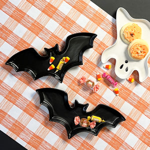 Madcap cottage black bat halloween plates and a white ghost halloween plate on an orange gingham paper table runner with halloween candies.