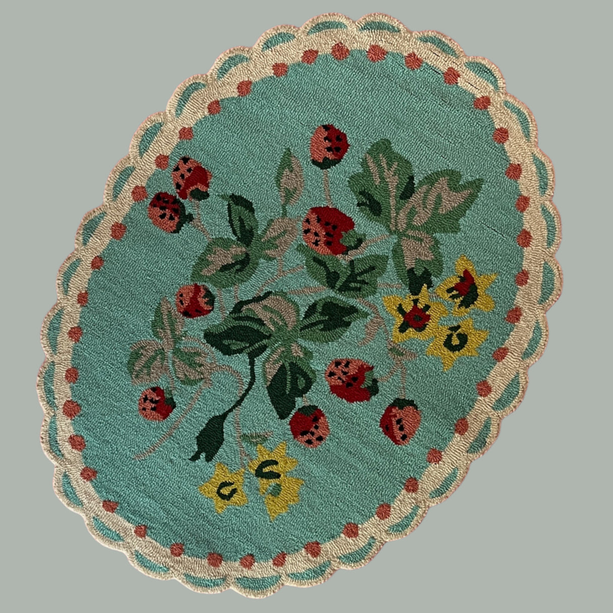 A blue oval rug with strawberry and flower motifs and a scalloped border
