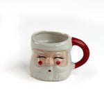 Ceramic Christmas santa mug with a jolly santa face design with red cheeks and a red handle on a white background