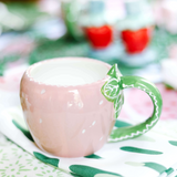 A pink strawberry mug in the shape of a strawberry with a green leafy handle sitting on a green and white napkin