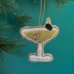 A green beaded martini Christmas ornament on a green background with pine leaves