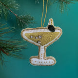 A green beaded martini Christmas ornament on a green background with pine leaves