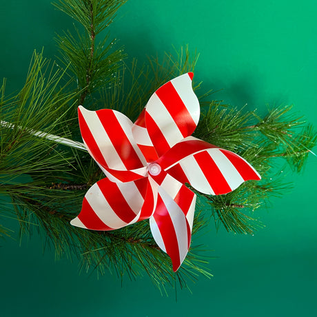 A red and white pinwheel decoration against a backdrop of a pine branch and green background