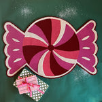 A Christmas rug in the shape of a wrapped red, white and pink candy. 