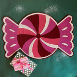A Christmas rug in the shape of a wrapped red, white and pink candy. 