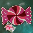 A Christmas rug in the shape of a wrapped red, white and pink candy. 