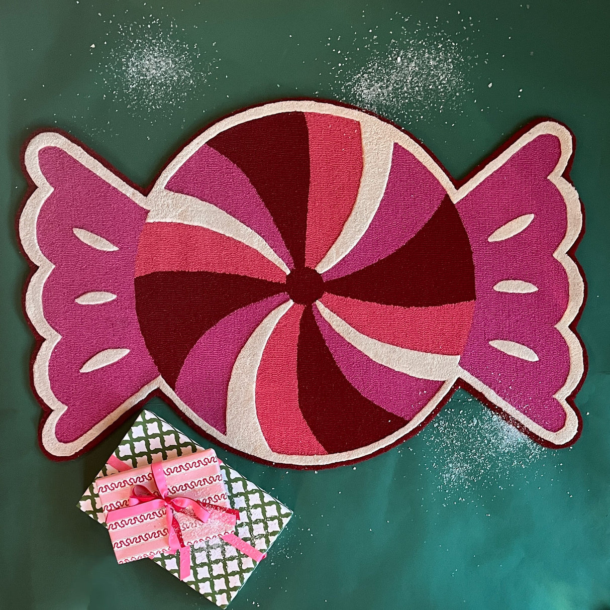 A Christmas rug in the shape of a wrapped red, white and pink candy. 
