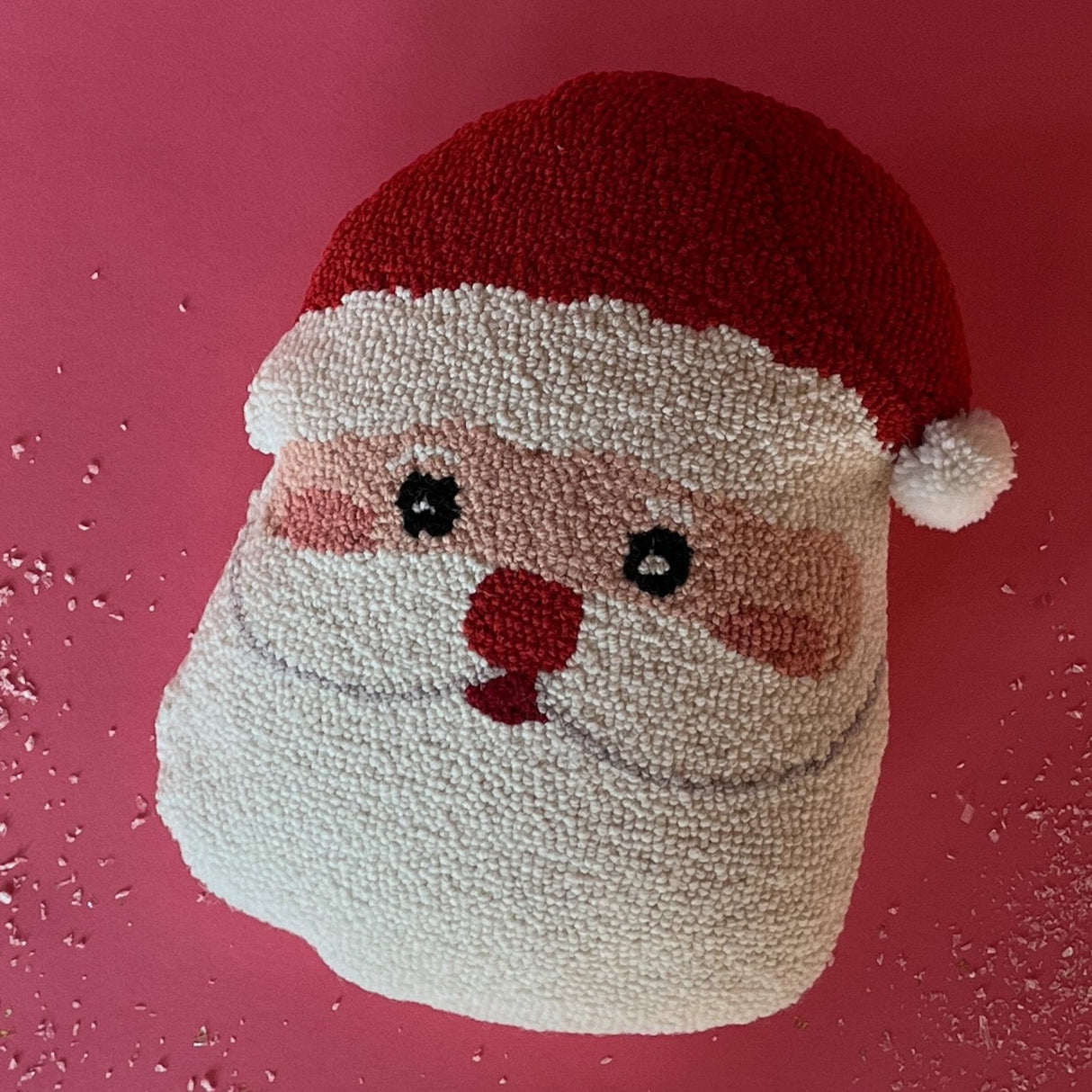 A hooked wool santa pillow in the shape of a friendly santa face