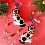 Two black and white staffodshire dog felt christmas ornaments against a red background.
