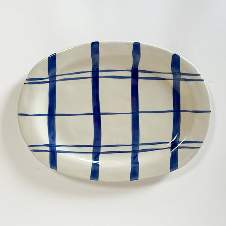 An oval shaped ceramic blue and white platter featuring a blue plaid pattern on white background. 