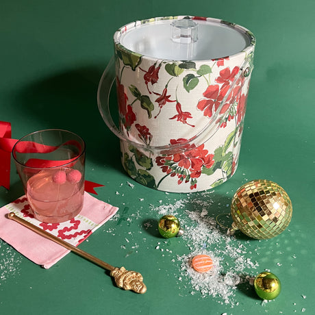 an acrylic ice bucket covered in geranium fabric and surrounded by a cocktail and festive decorations. 