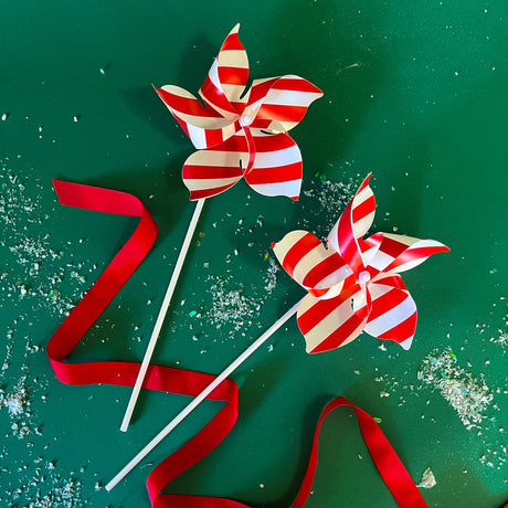 Two red and white pinwheel christmas decorations on a green background with a small sprinkle of snow and a red ribbon accent