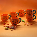 Madcap cottage six jack o'latern halloween coffee mugs on an orange background with halloween candy.