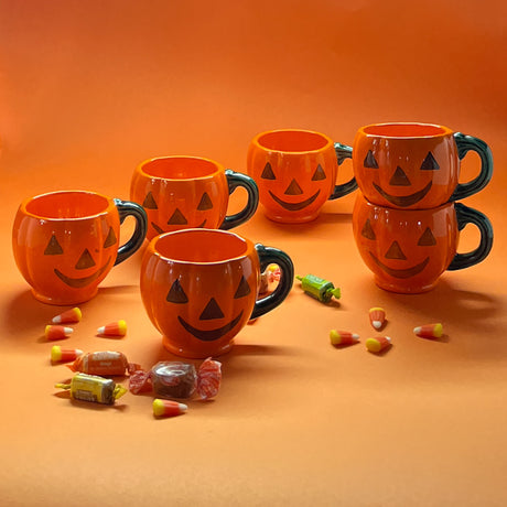 Madcap cottage six jack o'latern halloween coffee mugs on an orange background with halloween candy.