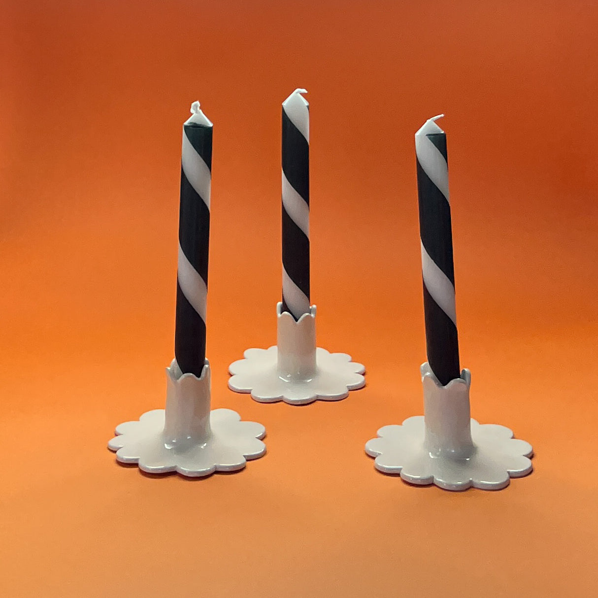 Madcap cottage halloween themed black and white taper candles in white ceramic stands on an orange background. 