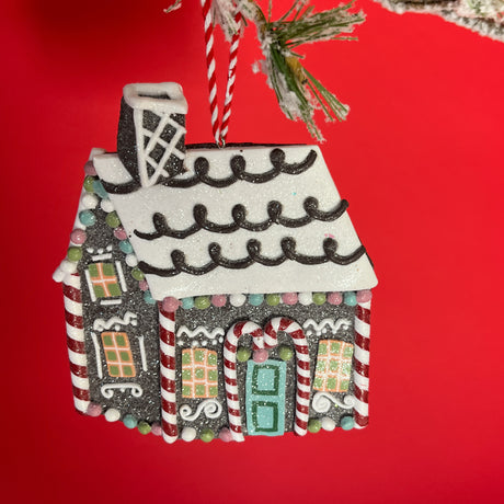 A brown gingerbread house ornament decorated with candy canes and sugar balls against a red background.