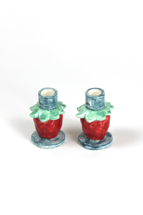 A pair of strawberry candle holders with a blue base and red strawberries forming the structure of the candle holder. 