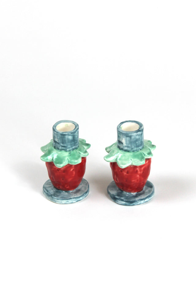 A pair of strawberry candle holders with a blue base and red strawberries forming the structure of the candle holder.