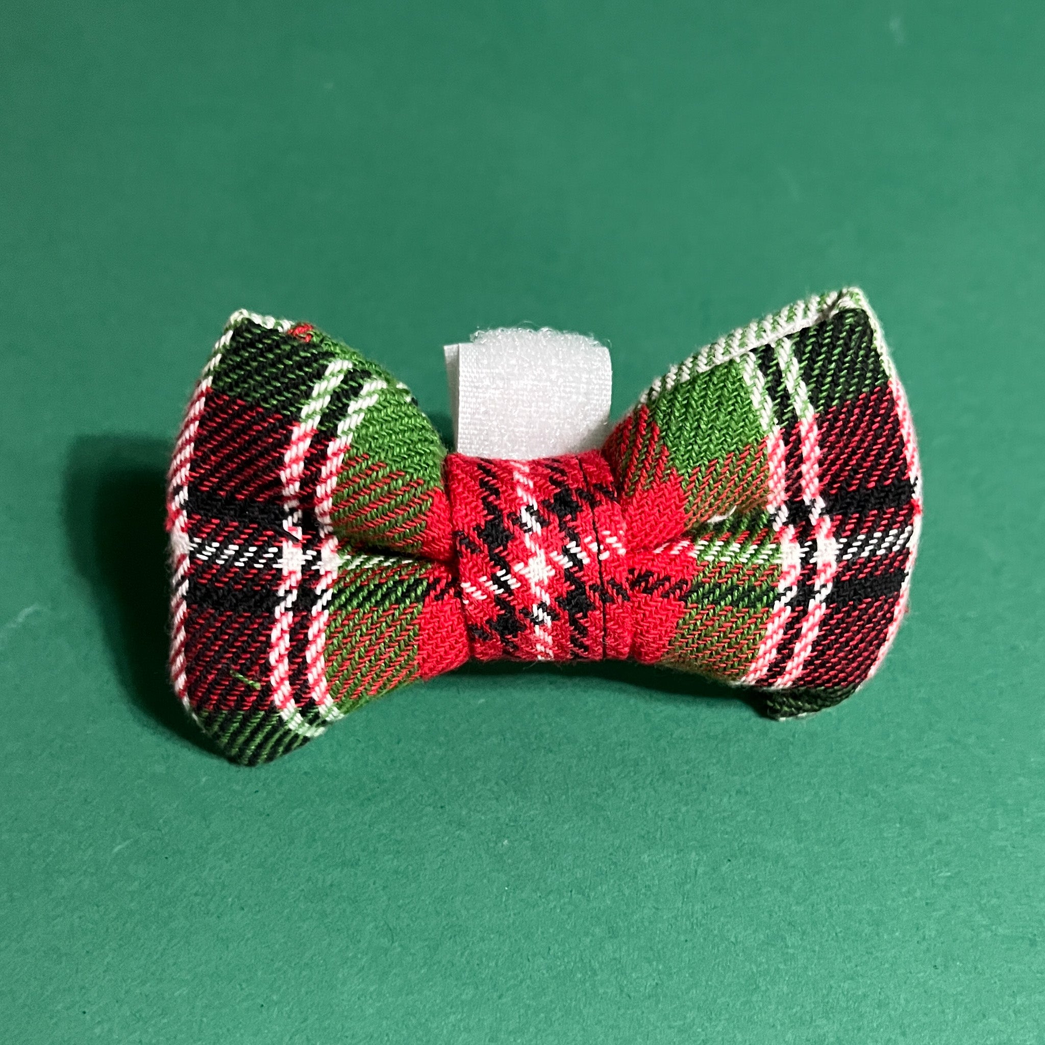 a McNixon Red/White/Dark Green Plaid Dog/Cat Bowties placed on a green surface