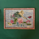 A small pink green and blue rug featuring waterlillies and heron motifs.